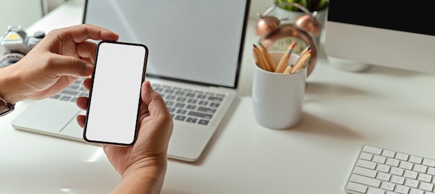Mann, der Modell-Smartphone auf Schreibtisch mit Modell-Laptop und Büromaterial verwendet