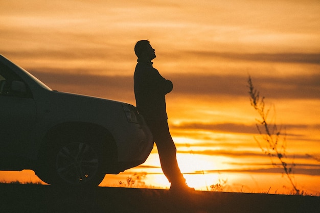 Mann, der nahe Auto auf Sonnenuntergangautoreisekonzept steht