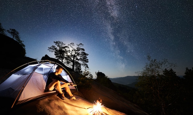 Mann, der neben Lagerfeuer und Touristenzelt in der Nacht ruht