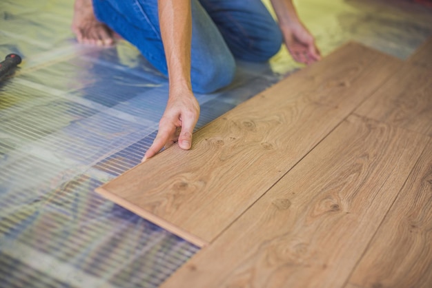 Mann, der neue Holzlaminatböden auf einem warmen Filmboden installiert. Infrarot-Fußbodenheizung unter Laminatboden