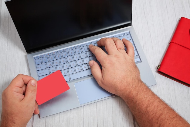 Mann, der online mit Kreditkarte und Laptop mit leerem Bildschirm einkauft Draufsicht auf menschliche Hände Laptop Tastatur Notebook auf weißem Holztisch Hintergrund Foto in hoher Qualität