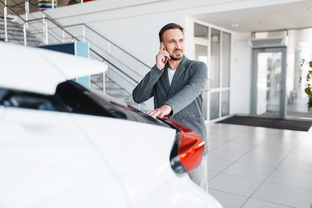 Mann, der per Telefon nahe dem neuen Auto im Ausstellungsraum spricht