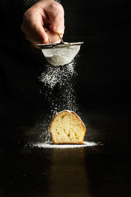 Mann, der puderzucker auf einen cupcake auf einem dunklen hintergrund besprüht