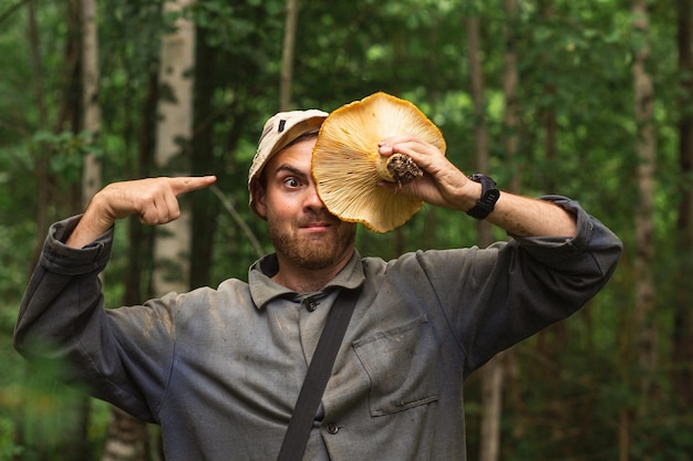 Mann, der riesigen Milchpilz vor seinem Gesicht hält, nachdem er sie an einem Herbsttag im Wald gepflückt hat