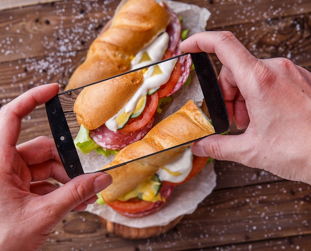 Mann, der Sandwich mit Wurst fotografiert