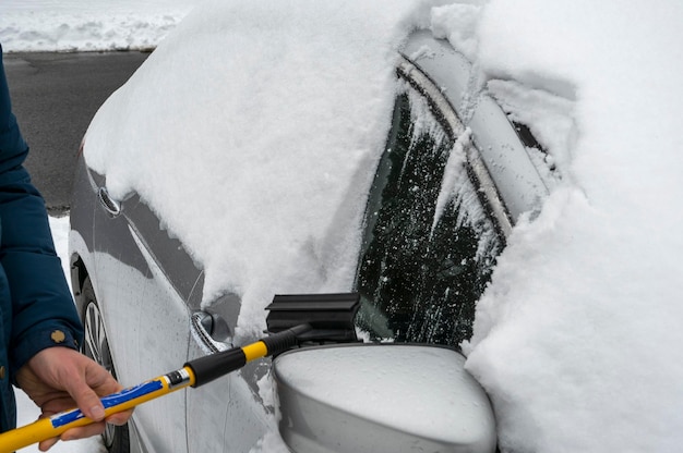 Mann, der Schnee von seinem Auto während des Winterschneefalls säubert