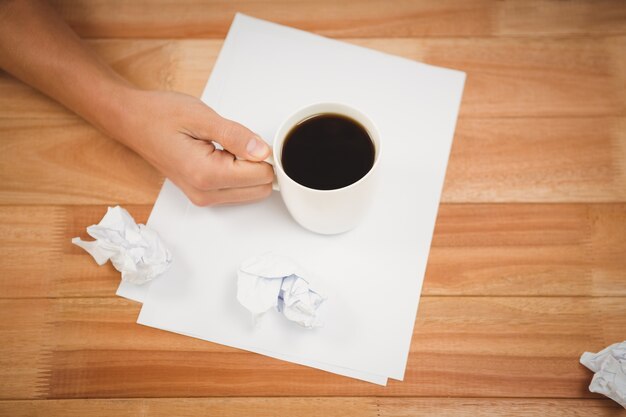 Mann, der schwarze Kaffeetasse auf Papier am Schreibtisch hält