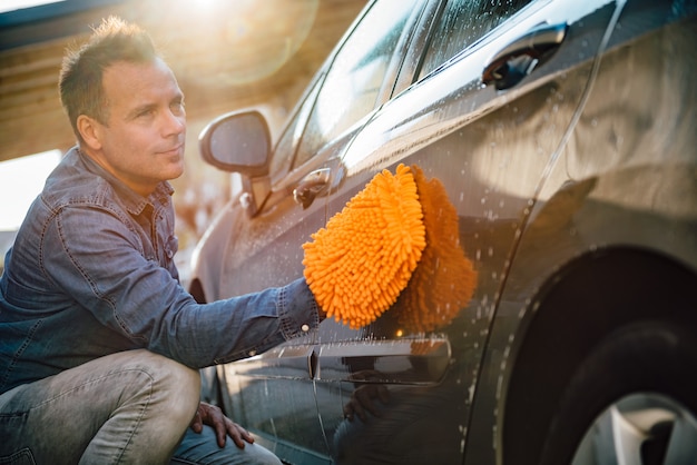 Mann, der sein Auto mit Waschhandschuh wäscht