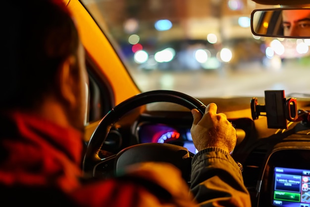 Mann, der sein Auto nachts mit unfokussierten Lichtern von anderen Fahrzeugen und der Stadt fährt