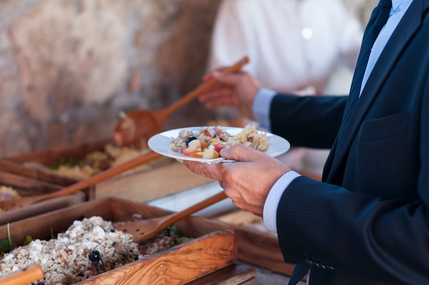 Mann, der sein Gericht mit Salat in Holztablett mit Löffel füllt