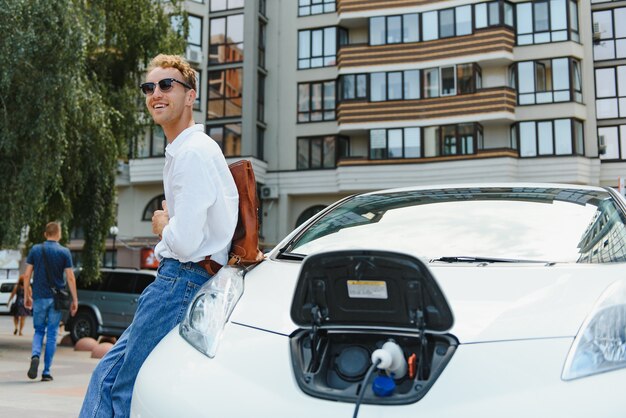 Mann, der sein luxuriöses Elektroauto an der Außenstation vor modernen neuen Stadtgebäuden auflädt