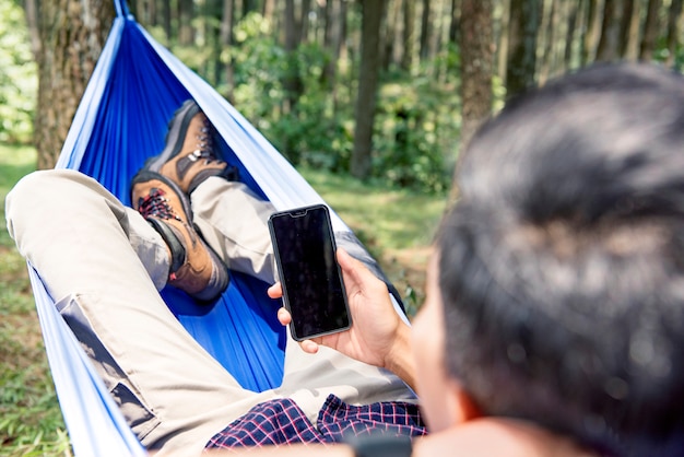 Mann, der seinen Handy bei der Entspannung in der Hängematte verwendet