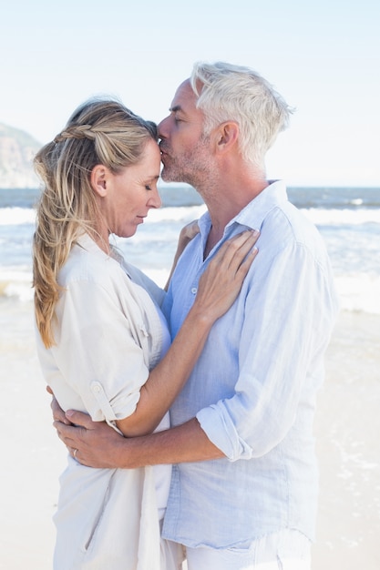 Mann, der seinen Partner auf der Stirn am Strand küsst