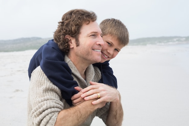 Mann, der seinen Sohn am Strand huckepack trägt