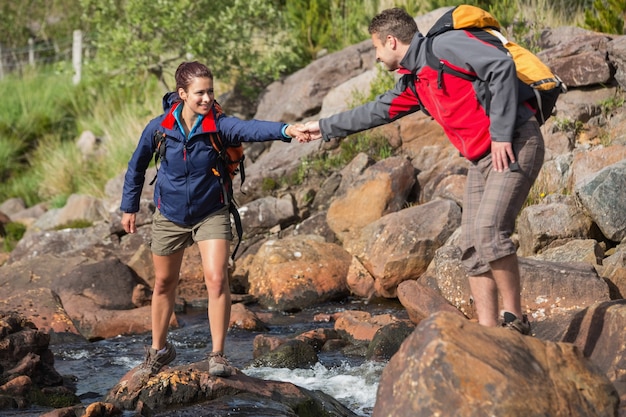 Mann, der seiner lächelnden Freundin hilft, einen Fluss zu kreuzen