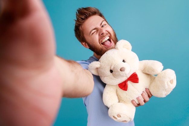 Mann, der Selfie macht oder Livestream-Sichtfoto sendet, hält Teddybär und lacht