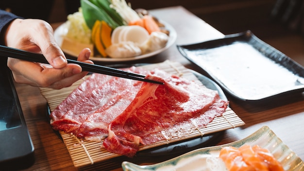 Mann, der seltenes Stück Wagyu A5 Rindfleisch durch Essstäbchen für das Kochen im heißen Topf von Shabu hält.