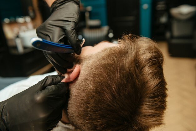 Mann, der sich vom Friseur Bart rasieren lässt, während er im Friseursalon im Stuhl liegt.