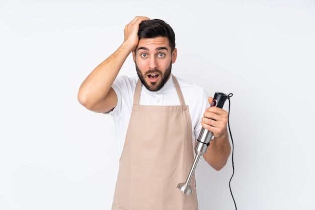 Mann, der Stabmixer auf weißer Wand mit überraschtem Gesichtsausdruck verwendet