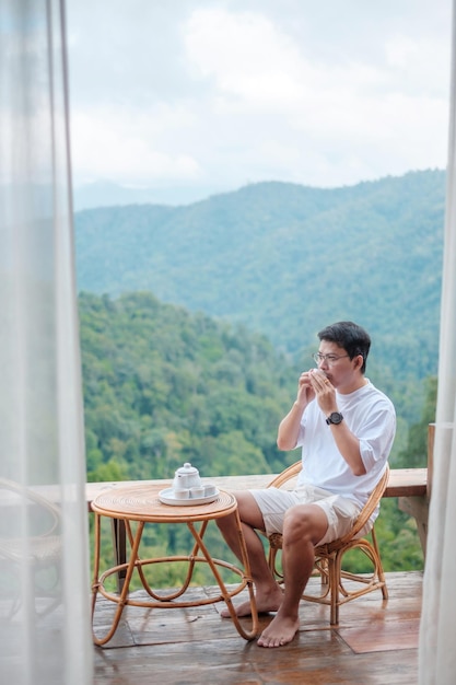 Mann, der Tee trinkt und Blick auf die Berge schaut, junger Tourist bleibt morgens in einer Gastfamilie auf dem Land Reiseurlaubsreise und entspannendes Konzept