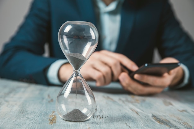 Mann, der Telefon mit Sanduhr auf Tisch hält