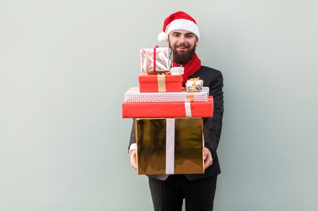 Mann, der viele Geschenkboxen hält und Kamera und zahniges Lächeln auf hellgrünem Hintergrund betrachtet