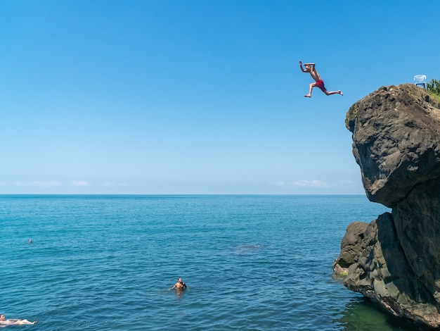 Mann, der vom hohen Felsen zum Meer springt