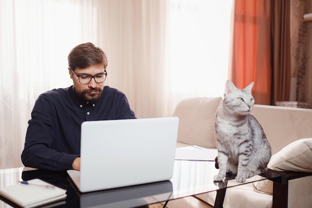 Mann, der von zu Hause aus am Laptop arbeitet Home Office mit Hauskatze