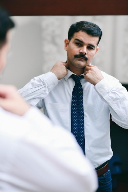 Mann, der vor Spiegel steht, trägt weißes Hemd und Krawatte indisches pakistanisches Modell