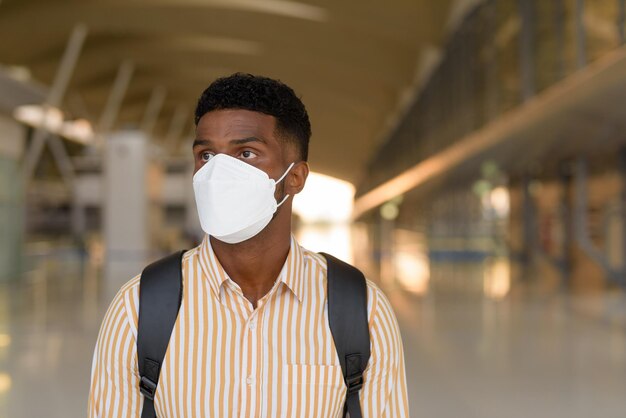 Mann, der während Covid am Flughafen reist und wartet und während der sozialen Distanzierung Gesichtsmaske trägt