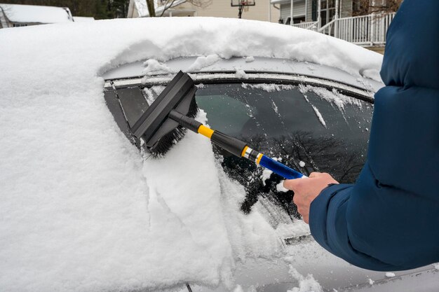 Mann, der während des Winterschneefalls Schnee von seinem Auto räumt Weiße Wintersaison