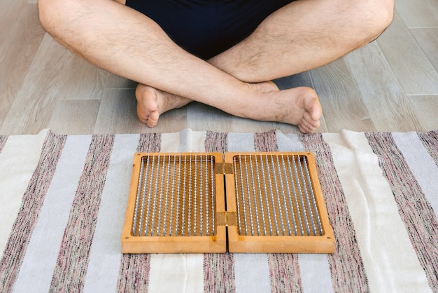 Mann, der Yoga meditiert, das sitzende Hände meditiert, verbunden auf dem Boden nahe einem sadhu Brett