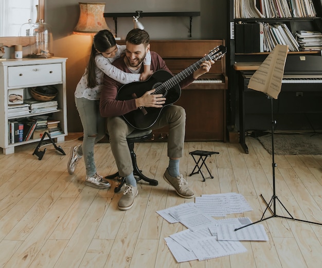 Mann, der zu Hause Akustikgitarre für Tochter im Wohnzimmer spielt