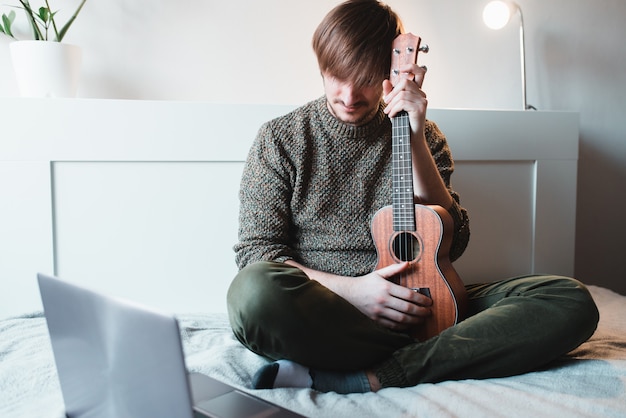 Mann, der zu Hause sitzt, lernt, Ukulele mit Online-Lektionen zu spielen.