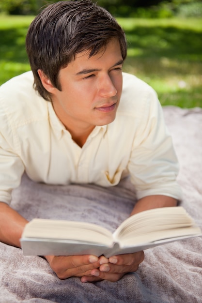 Mann, der zu seiner Seite beim Lesen eines Buches schaut, wie er auf einer Decke liegt