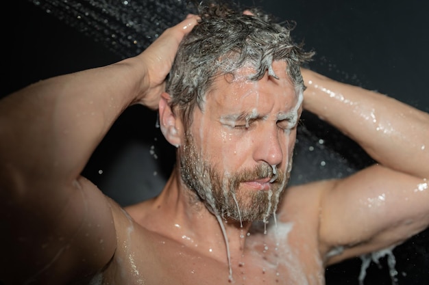 Mann duscht. Mann wäscht Haare mit Shampoo unter Wasser, das aus dem Duschkopf fällt. Morgenroutine