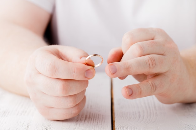 Mann entfernt einen goldenen Ehering von seinem Finger. Konzept des Familienstreites, der Scheidung oder des Verrats