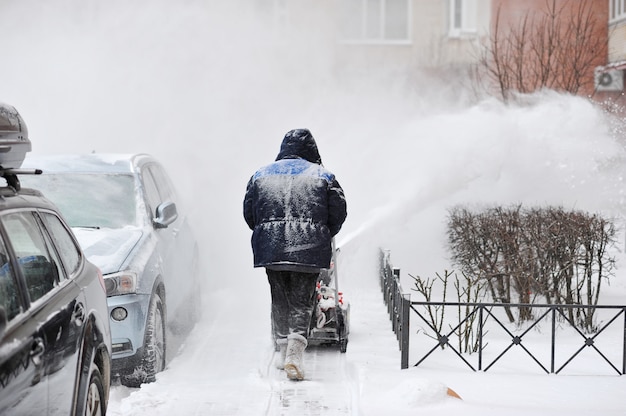 Mann entfernt Schnee im Yard eines mehrstöckigen Gebäudes mit Schneemaschinen