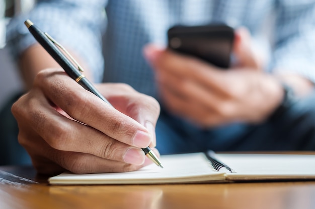 Mann etwas auf Notebook zu schreiben und Smartphone verwenden