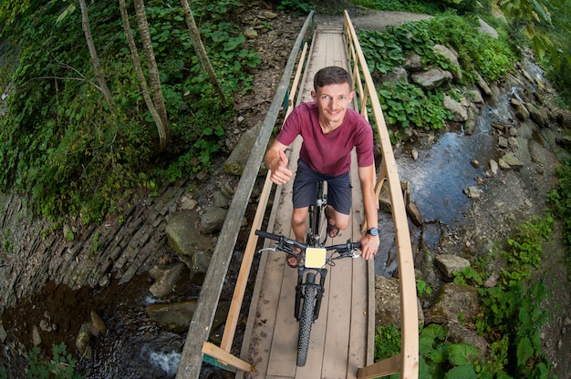 Mann fährt Fahrrad durch Holzbrücke über einen Fluss