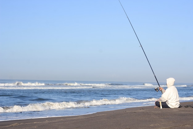 Mann fischt im Meer vom Strand aus