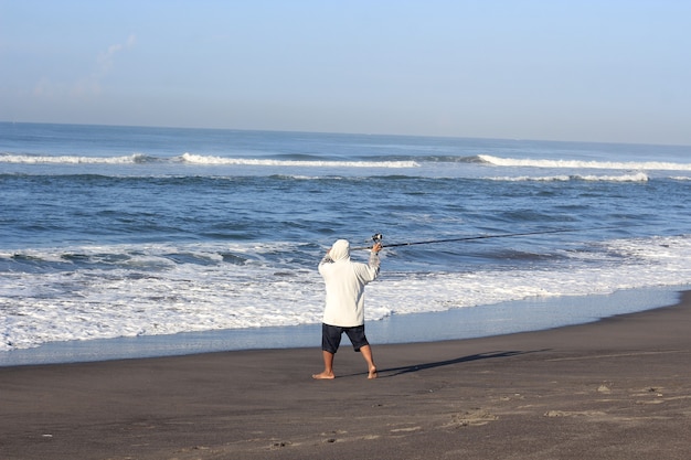 Mann fischt im Meer vom Strand aus