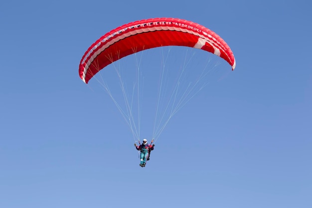 Mann fliegt unter einem roten Gleitschirm gegen einen blauen Himmel