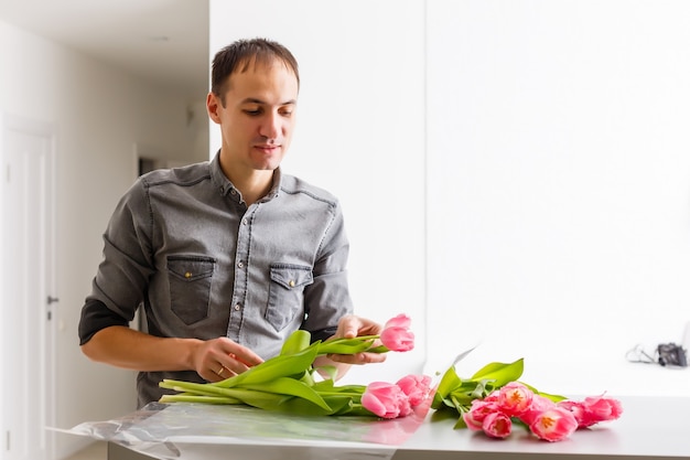 Mann Florist macht roten Tulpenstrauß und Verpackung auf Holztisch. Blumen