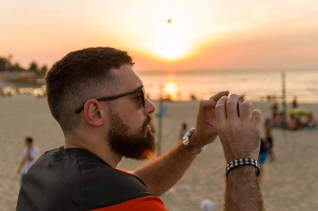 Mann fotografiert Sonnenuntergang am Strand mit Smartphone