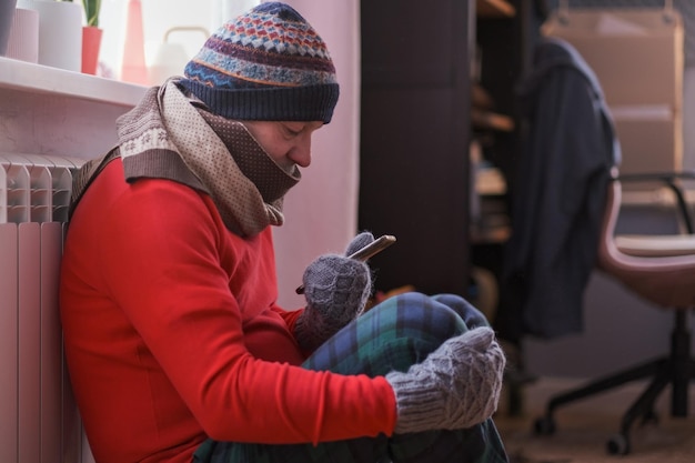 Mann fühlt sich zu Hause kalt und hat Probleme mit der Hausheizung, die mit dem Telefon sitzt.