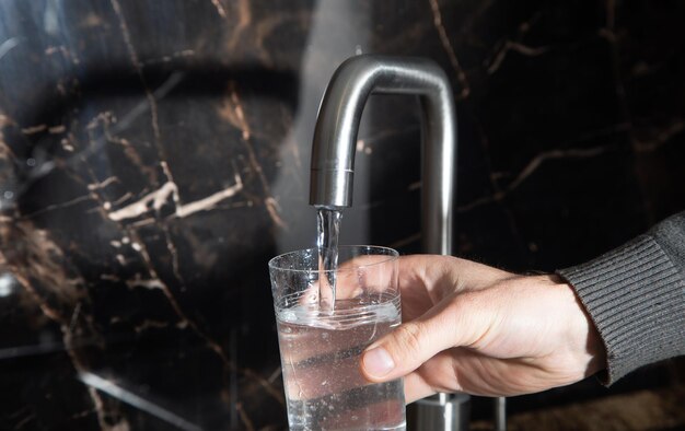 Mann füllt Glas mit Wasser aus dem Wasserhahn in der Küche