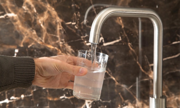 Mann füllt Glas mit Wasser aus dem Wasserhahn in der Küche