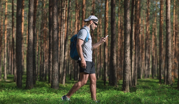 Mann geht in den Wald und benutzt ein Smartphone.