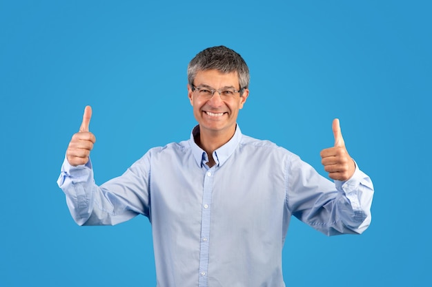 Mann gesteht mit beiden Händen auf blauem Hintergrund mit den Daumen nach oben